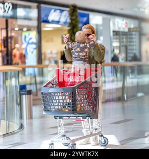 Mutter shoppt mit seinem Kind im Einkaufszentrum und hat Spaß. Mutter schiebt den Einkaufswagen mit ihrem Kleinkind, das in dem Korridor des Einkaufszentrums sitzt. Stockfoto