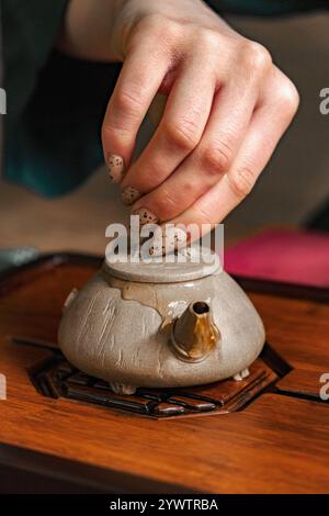 Eine elegante Hand legt den Deckel vorsichtig auf eine Teekanne für eine ruhige Teezeremonie Stockfoto