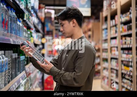 Chiang Mai, Thailand - 09. Dezember 2024: Ein gutaussehender asiatischer Mann, der in einem Supermarkt einkauft, Haushaltsartikel kauft und Produkte aus dem Regal auswählt. Nachteile Stockfoto
