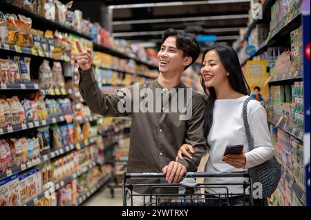 Chiang Mai, Thailand - 09. Dezember 2024: Ein glückliches junges asiatisches Paar genießt es, gemeinsam in einem Supermarkt einzukaufen, zu plaudern und Artikel aus dem Schalen auszuwählen Stockfoto