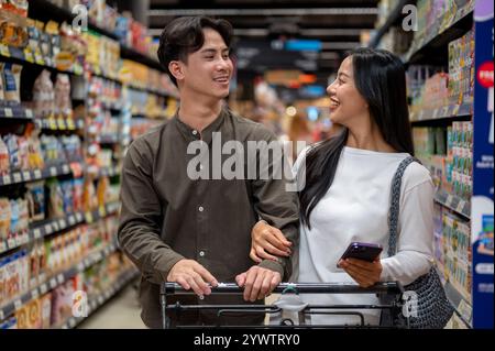 Chiang Mai, Thailand - 09. Dezember 2024: Ein glückliches junges asiatisches Paar genießt es, gemeinsam in einem Supermarkt einzukaufen, zu plaudern und Artikel aus dem Schalen auszuwählen Stockfoto