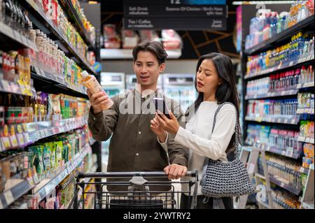 Chiang Mai, Thailand - Dez 09 2024: Ein nettes junges asiatisches Paar, das zusammen in einem Supermarkt shoppt, Artikel aus den Regalen auswählt und das überprüft Stockfoto