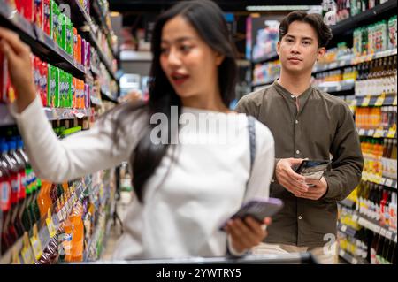 Chiang Mai, Thailand - 09. Dezember 2024: Ein glückliches junges asiatisches Paar genießt es, gemeinsam in einem Supermarkt einzukaufen, zu plaudern und Artikel aus dem Schalen auszuwählen Stockfoto