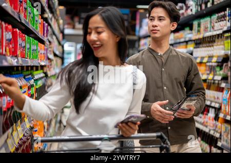 Chiang Mai, Thailand - 09. Dezember 2024: Ein glückliches junges asiatisches Paar genießt es, gemeinsam in einem Supermarkt einzukaufen, zu plaudern und Artikel aus dem Schalen auszuwählen Stockfoto