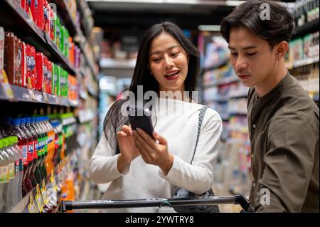 Chiang Mai, Thailand - Dez 09 2024: Ein nettes junges asiatisches Paar, das zusammen in einem Supermarkt shoppt, Artikel aus den Regalen auswählt und das überprüft Stockfoto