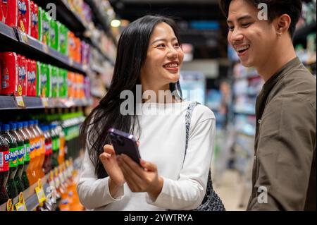 Chiang Mai, Thailand - Dez 09 2024: Ein nettes junges asiatisches Paar, das zusammen in einem Supermarkt shoppt, Artikel aus den Regalen auswählt und das überprüft Stockfoto