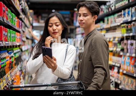 Chiang Mai, Thailand - Dez 09 2024: Ein nettes junges asiatisches Paar, das zusammen in einem Supermarkt shoppt, Artikel aus den Regalen auswählt und das überprüft Stockfoto