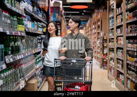 Chiang Mai, Thailand - 09. Dez 2024: Ein süßes, glückliches junges asiatisches Paar, das in einem Supermarkt einkauft, nach Artikeln sucht und Spaß am Chatten hat Stockfoto