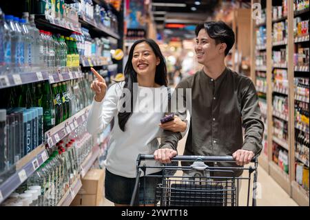 Chiang Mai, Thailand - 09. Dez 2024: Ein süßes, glückliches junges asiatisches Paar, das in einem Supermarkt einkauft, nach Artikeln sucht und Spaß am Chatten hat Stockfoto
