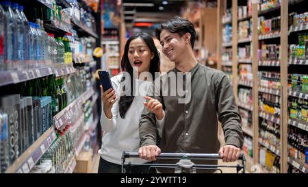 Chiang Mai, Thailand - Dez 09 2024: Ein nettes junges asiatisches Paar, das zusammen in einem Supermarkt shoppt, Artikel aus den Regalen auswählt und das überprüft Stockfoto