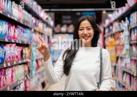 Chiang Mai, Thailand - Dez 09 2024: Eine schöne asiatische Frau, die in einem Supermarkt einkauft, mit einem Einkaufswagen in einem Gang steht und den Camer anlächelt Stockfoto