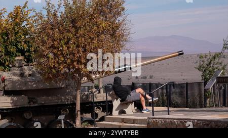 GOLANHÖHEN, ISRAEL – 11. DEZEMBER: Ein israelischer Zivilist sitzt neben einem verlassenen Panzer in einem Aussichtspunkt in der Nähe von Quneitra und überquert die Grenze zu Syrien in den israelischen Golanhöhen, während die israelische Armee am 11. Dezember 2024 ihre Bodenkräfte in der syrischen Pufferzone in Golanhöhen, Israel, verstärkt. Stockfoto