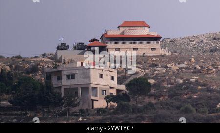 GOLANHÖHEN, ISRAEL – 11. DEZEMBER: Fernsicht der israelischen Flagge und der israelischen Panzer vor einem Haus am Rande des syrischen Dorfes Hader, während die israelische Armee am 11. Dezember 2024 ihre Bodenkräfte in der syrischen Pufferzone in Golanhöhen, Israel, verstärkt. Stockfoto