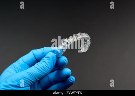 In der Hand hält eine Person, die blaue Handschuhe trägt, eine klare Klammer. Das Bild könnte Konzepte wie Gesten, Finger, Musikinstrument und vieles mehr hervorrufen Stockfoto