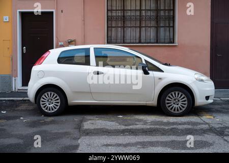 Cremona, Italien - 27. November 2024 Weißer Fiat grande Punto 1,2 parkt auf der Straße in der Nähe eines Wohnhauses mit rosa Fassade Stockfoto