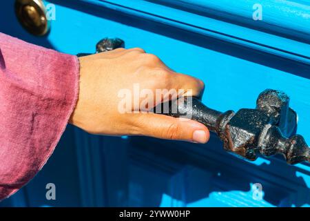 Eine Frau, die einen alten Metalltürgriff einer blauen Tür hält. Öffnen der Tür. Stockfoto
