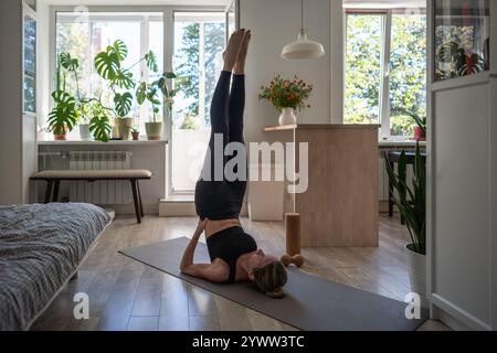 Die Frau hält die Schulterposition Sarvangasana, liegend auf dem Rücken, die Beine senkrecht angehoben und die Hände stützen sie. Stockfoto