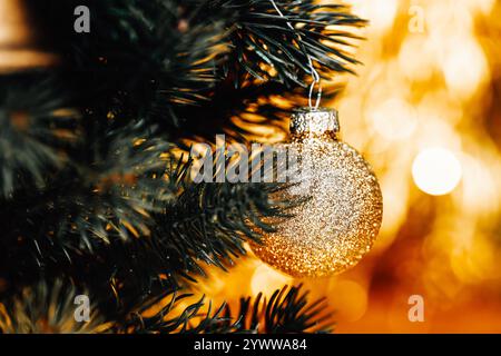 Glitzernde Weihnachtskugel hängt am Baum, goldener und grüner Weihnachtshintergrund, Detail auf goldener Weihnachtskugel Stockfoto