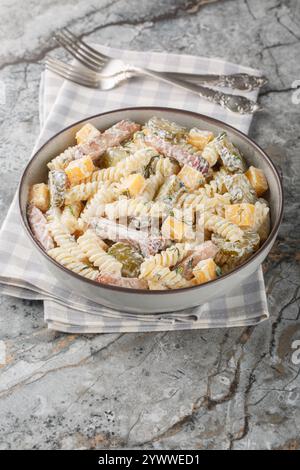Fusilli-Nudelsalat mit Gurken, Cheddar-Käse, Dill und Speck mit Sahnesauce in einer Schüssel auf dem Tisch. Vertikal Stockfoto