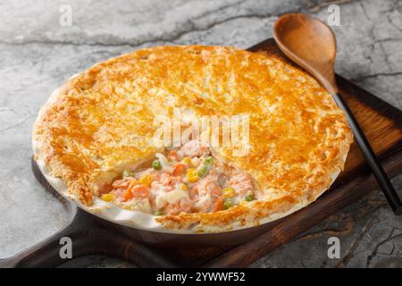 Hausgemachter Salmon Pot Pie mit Karotten, Mais, Zwiebeln und Erbsen und in einer Butterkruste auf der Auflaufform auf dem Tisch. Horizontal Stockfoto
