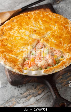 Lachs Pot Pie aus frischen Lachsfilets, gemischtem Gemüse, einer cremigen Sauce und einem knusprigen Blätterteigdeckel in der Nähe auf der Auflaufform auf der Registerkarte Stockfoto