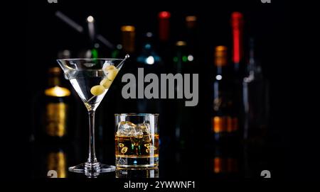 Martini Cocktail und Whiskey auf den Felsen auf einem Bartisch. Das farbenfrohe Bokeh der beleuchteten Flaschen im Hintergrund verbessert die Stimmung und sorgt für einen Dye Stockfoto