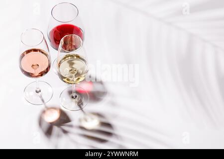 Drei Weingläser gefüllt mit Rot-, weiß- und Rosenwein, anmutig auf einem hellen, minimalistischen Hintergrund. Eine lebendige Darstellung der Vielfalt der Weine Stockfoto