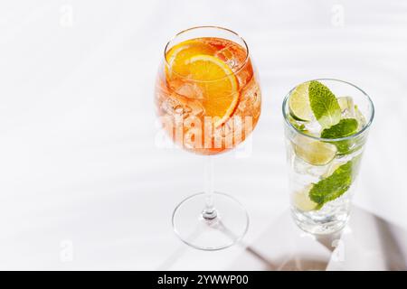 Ein lebendiger Aperol-Spritz und Mojito-Cocktails in einem Glas, das wunderschön präsentiert wird, vor einem hellen weißen Hintergrund Stockfoto