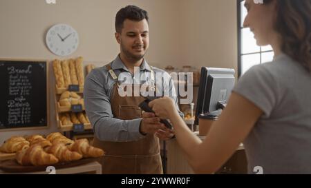 Frau bezahlt mit Karte an einen lächelnden Mann in einer Bäckerei voller Croissants und Baguettes Stockfoto