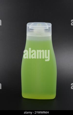 Klare, weiße matte Flasche mit Spender, Kosmetikprodukt. Eine mit einer hellgrünen, grünen Flüssigkeit gefüllte Kunststoffflasche befindet sich auf einem schwarzen Kunststoff. Stockfoto