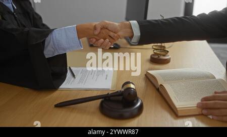 Mann und Richter schütteln sich die Hand in einem Anwaltsbüro nach einer erfolgreichen Vereinbarung, mit juristischen Dokumenten, einem Hammer und einer Waage auf dem Schreibtisch, die einen zeigt Stockfoto