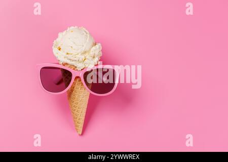 Ein verspielter Eisbecher mit stylischer Sonnenbrille vor einem leuchtend rosa Hintergrund, der Sommeratmosphäre und Spaß verströmt Stockfoto