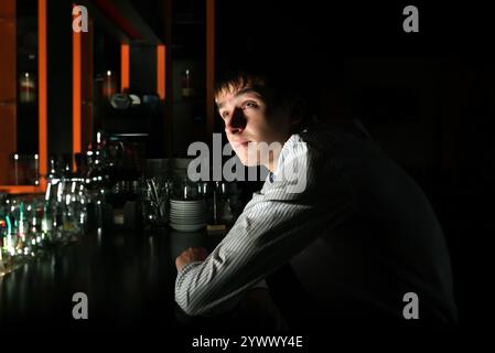 Junger Mann, der in der Dunkelheit in der Bar sitzt Stockfoto