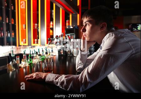 Trauriger und einsamer junger Mann, der in der Dunkelheit an der Bar sitzt Stockfoto