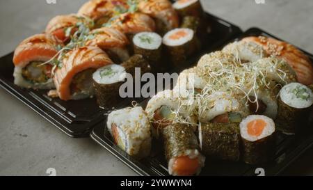 Verschiedene Sushi-Brötchen auf Tabletts mit Lachs und Algen auf einer Betonoberfläche, die köstliche japanische Küche zeigt Stockfoto