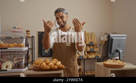 Junger Mann, der mit seinen Händen in einer Bäckerei mit verschiedenen frisch gebackenen Waren und Gebäck eine Geste macht. Stockfoto