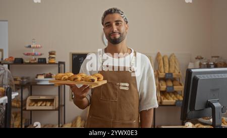 Hübscher junger arabischer Mann mit Bart, der ein Tablett mit Gebäck in einer Bäckerei hält. Stockfoto