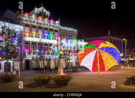 Águeda, Portugal - 27. November 2024: Nächtlicher Blick auf Gebäudefassaden, die mit Weihnachtslichtern und einem riesigen Sonnenschirm mit Lichtern auf dem Platz dekoriert sind. Stockfoto