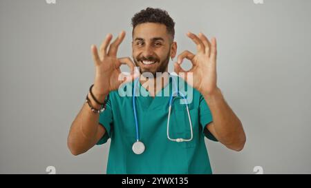 Junger hispanischer Mann in blaugrün schrubbt, der selbstbewusst mit OK-Geste lächelt, isoliert auf weißem Hintergrund, verkörpert professionelles Gesundheitsbild. Stockfoto