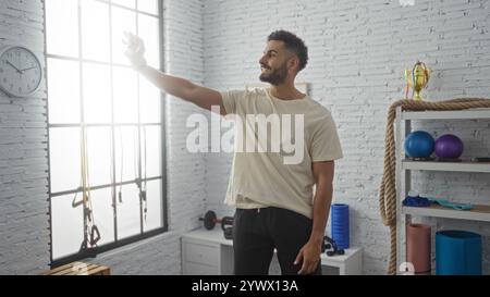 Junger gutaussehender hispanischer Mann, der ein Selfie in einer Turnhalle mit Trainingsgeräten im Hintergrund macht Stockfoto