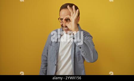 Hübscher hispanischer Mann, der eine gute Geste mit der Hand vor dem Auge macht, vor einem isolierten gelben Hintergrund. Stockfoto