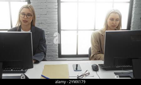 Zwei Geschäftsfrauen arbeiten an Computern in einem modernen Büro mit Papierkram und digitalen Geräten und präsentieren eine professionelle Geschäftsumgebung im Innenbereich. Stockfoto