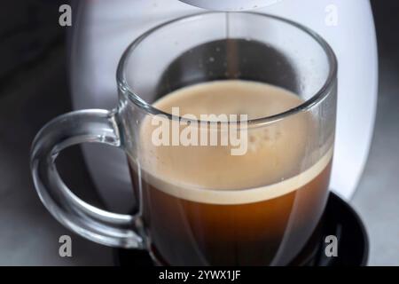 Kaffeemaschine, elektrisches Gerät, das schwarzes Americano-Getränk in einen Becher aus Glas gießt Stockfoto