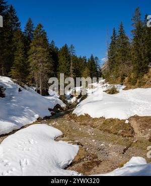 In Garmisch-Partenkirchen im Winter bedeckt Schnee die Landschaft. Ein sich windender Bach fließt sanft durch das Tal, umgeben von üppigem, immergrünem t Stockfoto