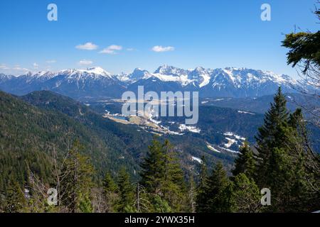 Atemberaubende Aussicht auf Garmisch-Partenkirchen, Bayern, mit schneebedeckten Gipfeln und üppig grünen Wäldern unter klarem blauem Himmel im Winter. Die Ruhe Stockfoto