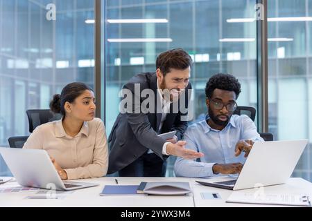 Ein Manager spricht frustriert zwei Mitarbeiter während eines Arbeitsgesprächs in einem modernen Büro an. Stockfoto