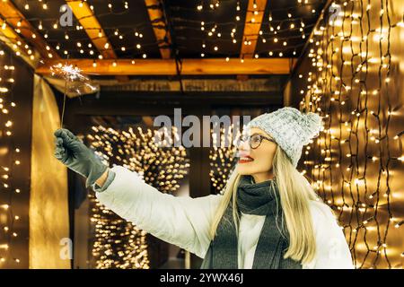 Eine junge Frau, die einen Funkler mit festlichen Lichtern hält Stockfoto