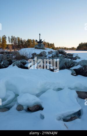 Ein ruhiger Wintertag in Leksand, Dalarna, zeigt ein felsiges Ufer, das teilweise mit Schnee bedeckt ist. Das ruhige gefrorene Wasser spiegelt die friedliche Atmosphäre wider Stockfoto