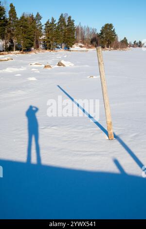 Im verschneiten Gelände von Västanvik, Dalarna, wird im Winter ein hoher Schatten von einer Person geworfen, die auf dem gefrorenen Boden steht. Das Sonnenlicht erzeugt ein starkes Licht Stockfoto