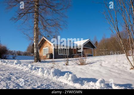 Eine charmante Hütte in der schneebedeckten Landschaft von Västanvik, Dalarna im Winter. Heller Sonnenschein unterstreicht die ruhige Schönheit der Umgebung Stockfoto